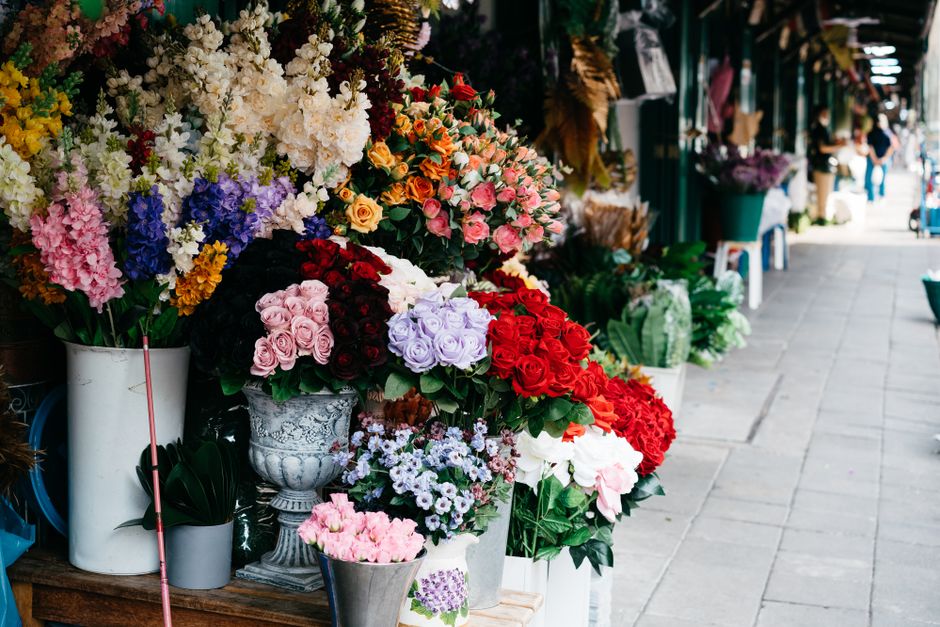 A vibrant display of fresh flower arrangements outside a florist shop, featuring a variety of blooms including pink and white roses, deep red roses, purple hydrangeas, and multicolored mixed flowers a